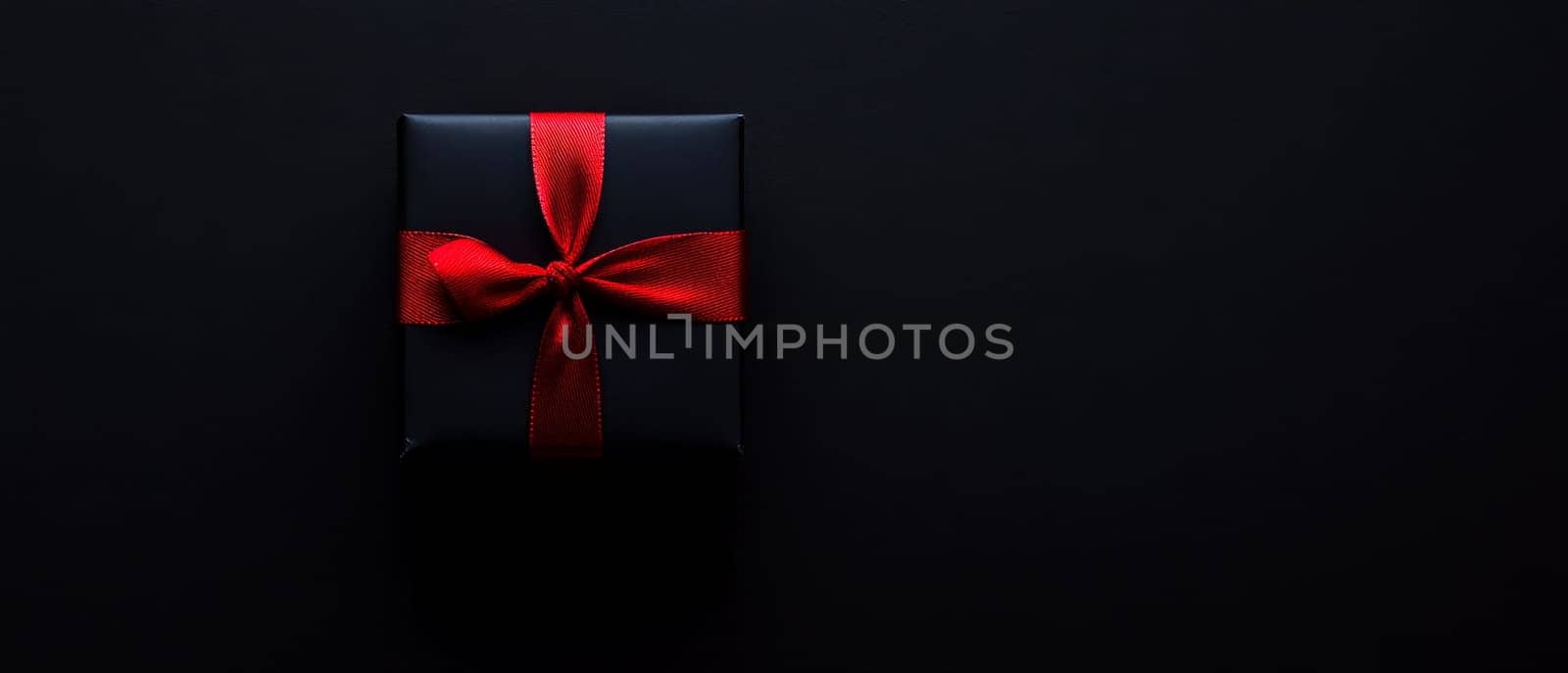 Simple black gift box tied with a striking red ribbon, emphasizing elegance and minimalism on a dark background.