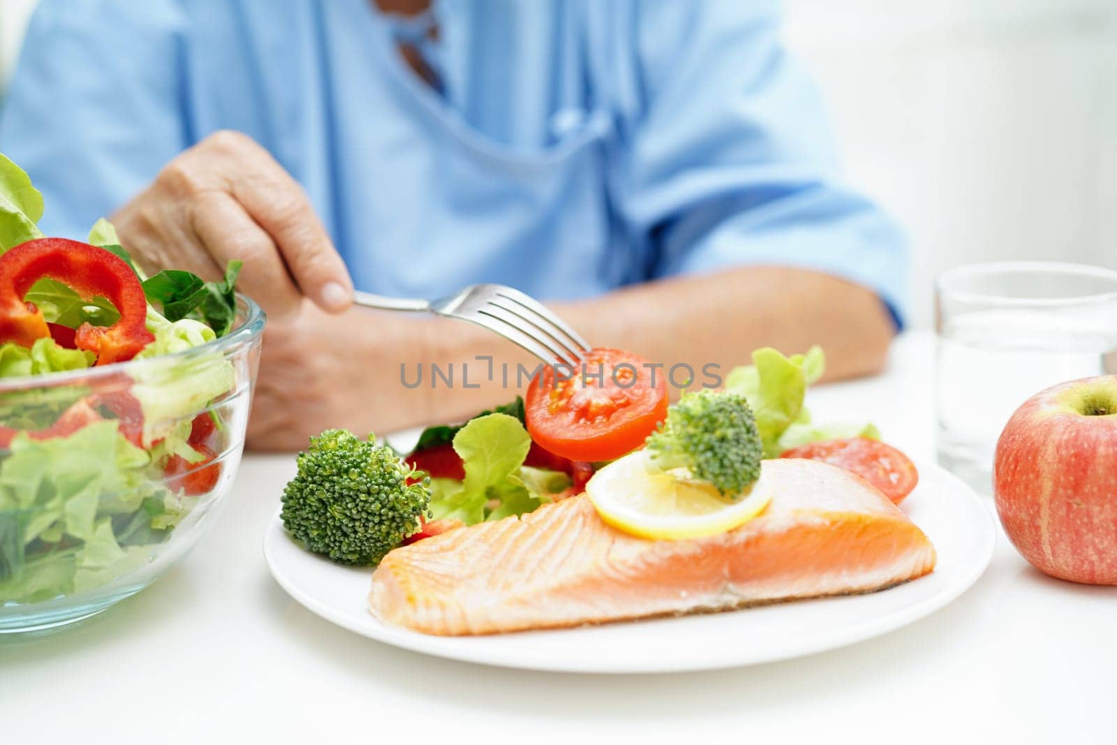 Asian elderly woman patient eating salmon stake and vegetable salad for healthy food in hospital.