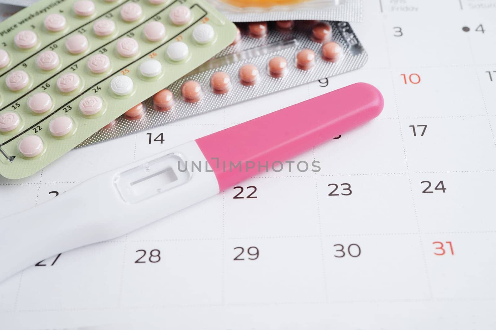 Pregnancy test with birth control pills and condom for female on calendar, ovulation day.