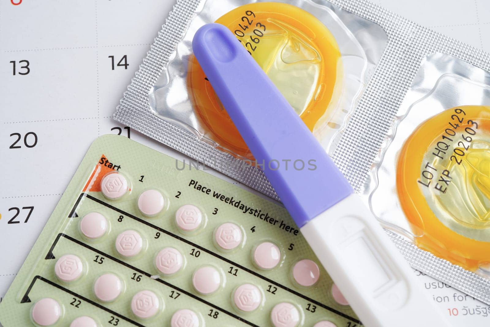 Pregnancy test with birth control pills and condom for female on calendar, ovulation day.