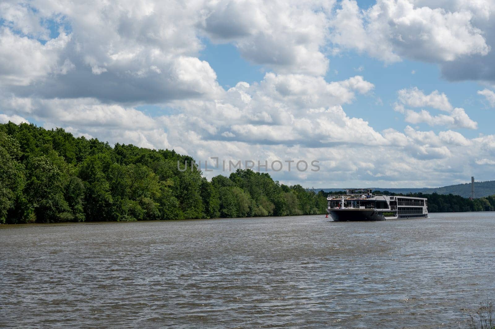 A pleasure boat sails along a river, with green nature, blue sky and white clouds