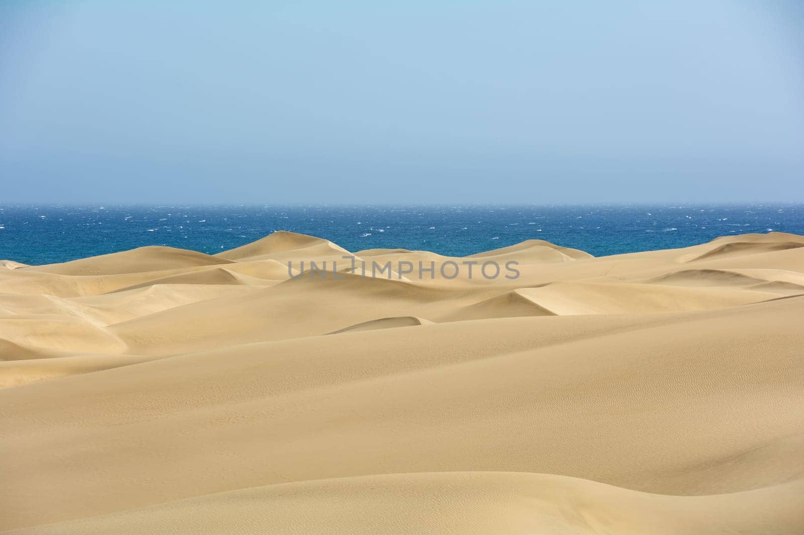 The dunes of Maspalomas on Gran Canaria in Spain, with sea and blue sky. The huge sand dunes resemble a small desert and are a nature reserve.