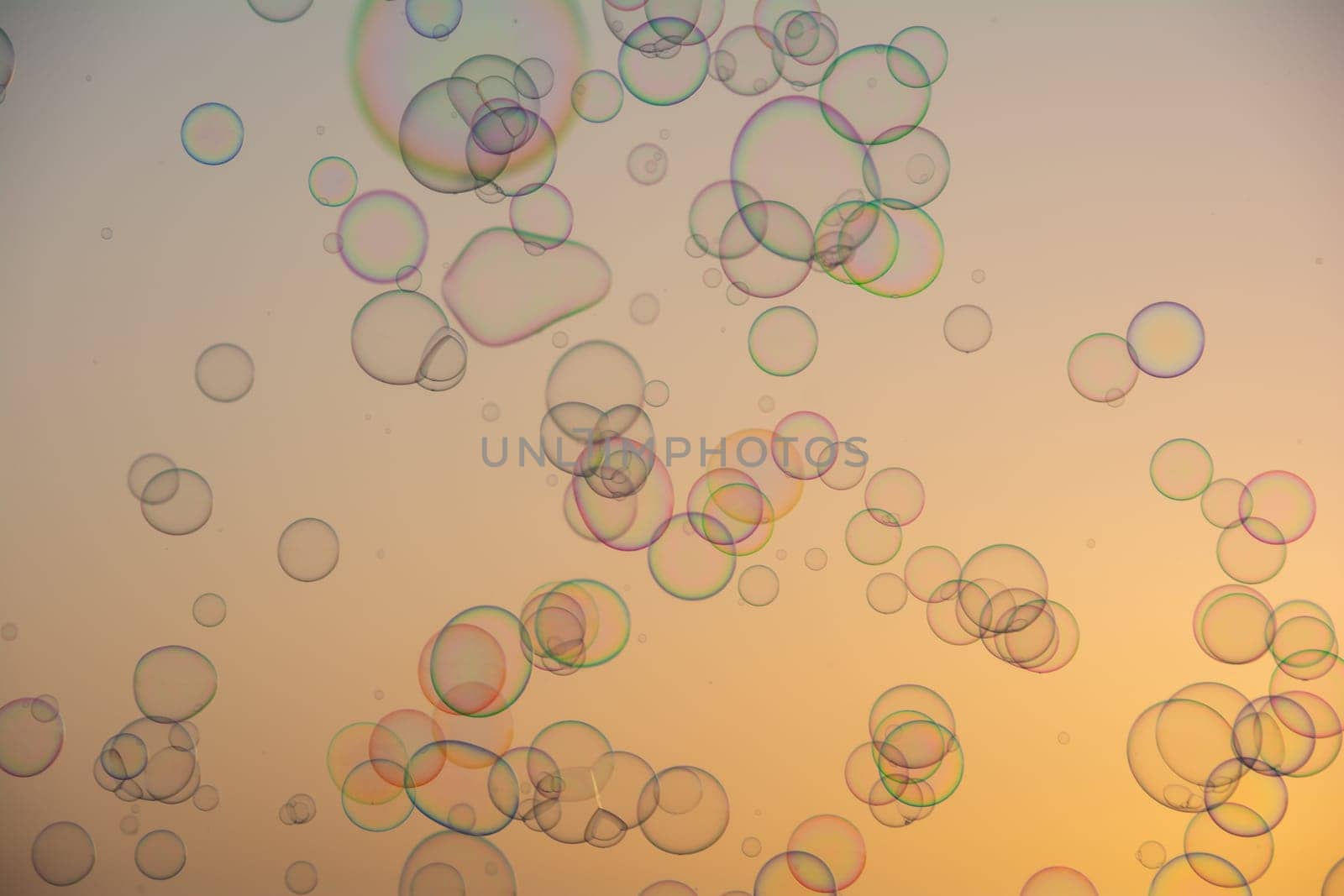 Many colorful soap bubbles float in the orange sky at sunset