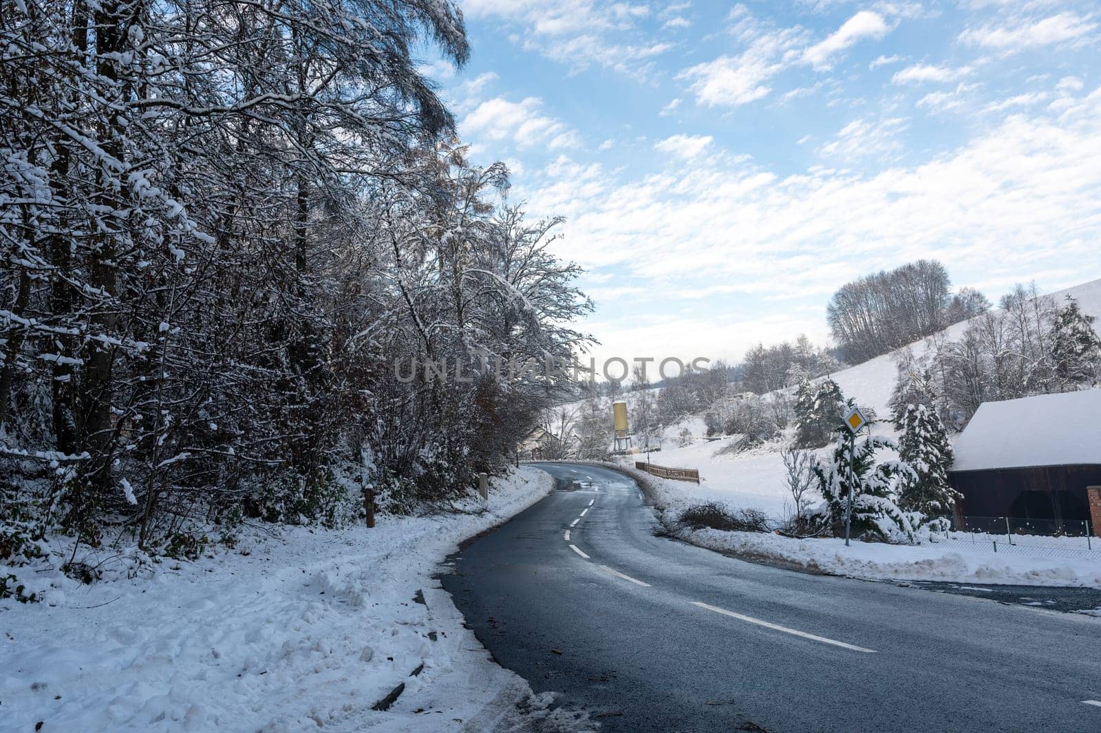 Snow landscape with trees, road and blue sky with clouds