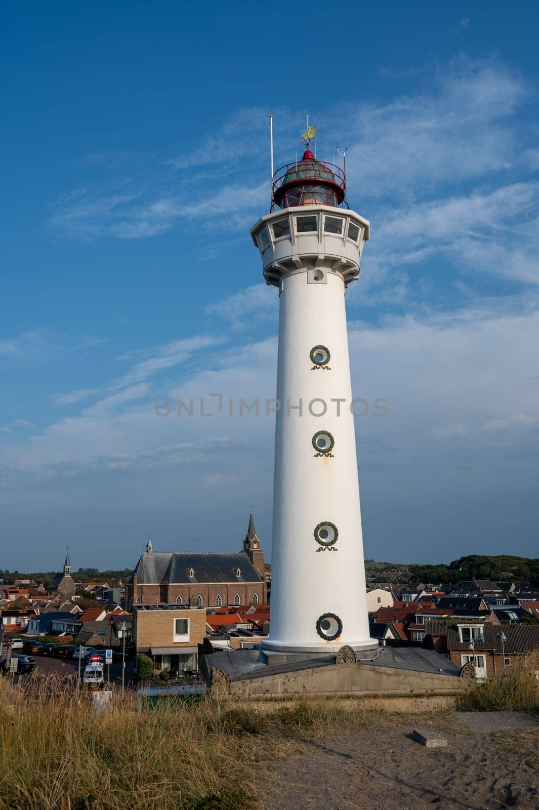 The approx. 28 m high white lighthouse J.C.J. van Speijk in Egmond aan Zee, North Holland, Netherlands with some of the town's houses
