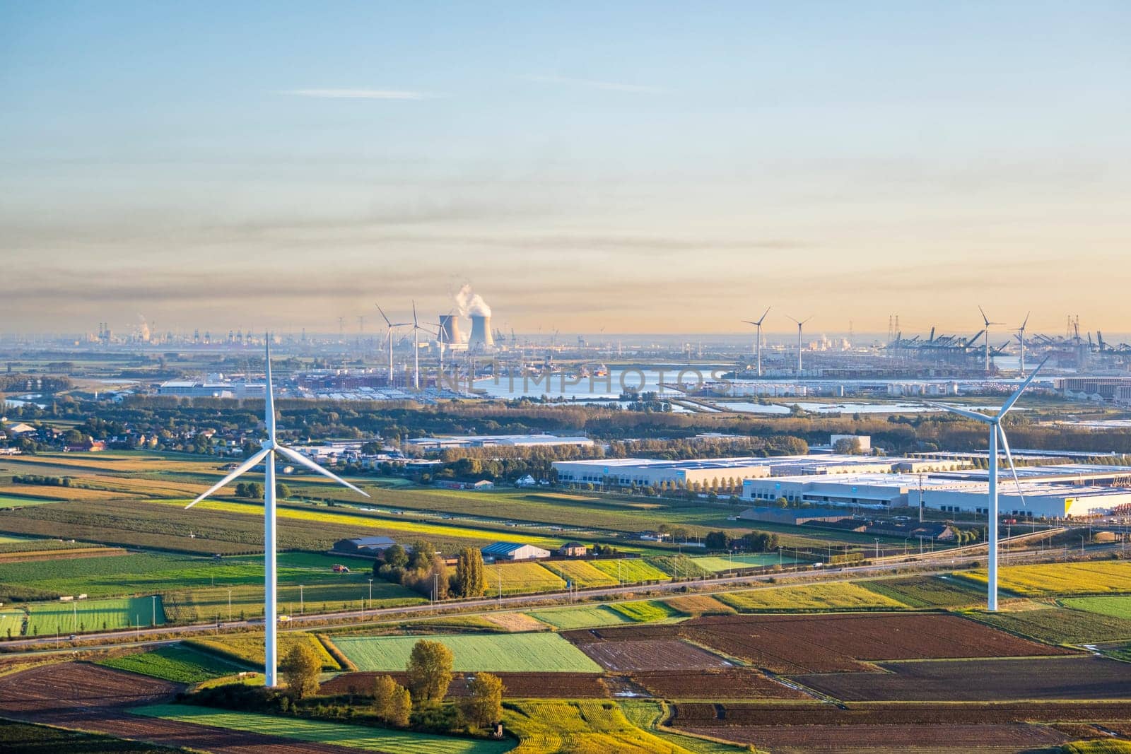 Beveren, Belgium, September 29th 2024: Aerial view on Waasland rural patchwork farmland area mixed with wind turbines and harbor of Antwerp in the far distance during sunrise