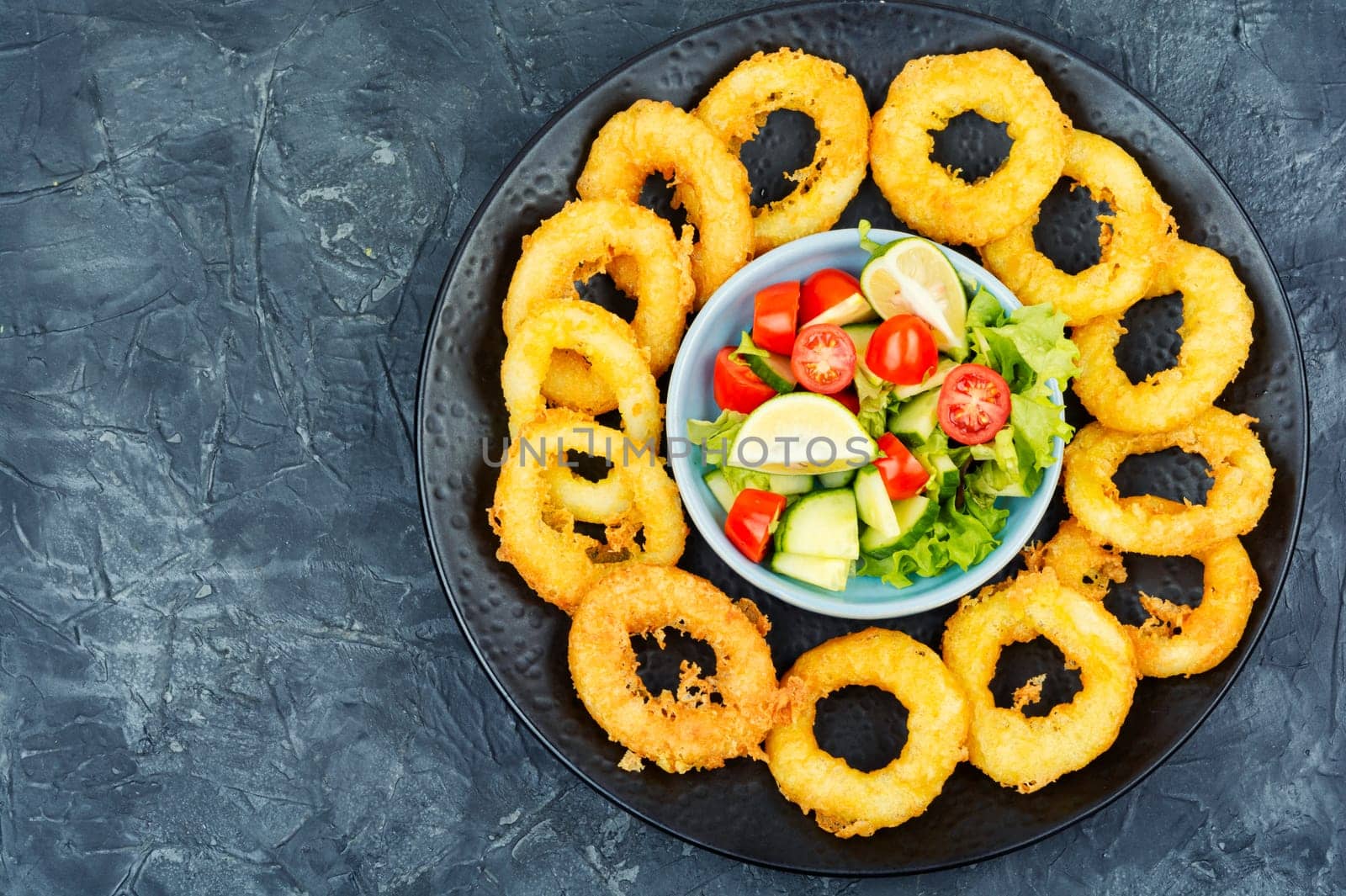 Delicious Fried squid rings and fresh vegetable salad on stone table background. Copy space.