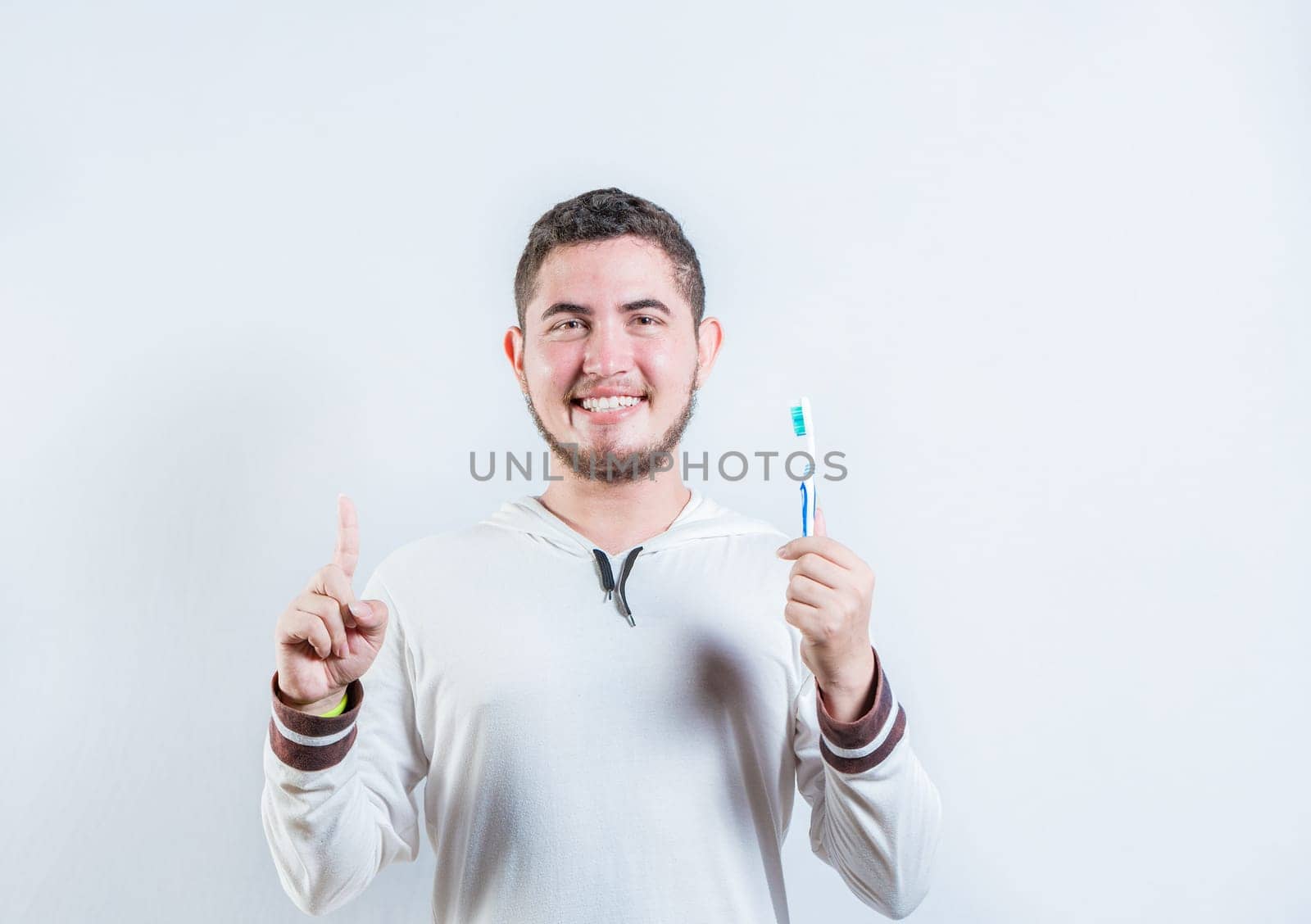 Positive young man holding toothbrush pointing up. Happy guy holding toothbrush and pointing up