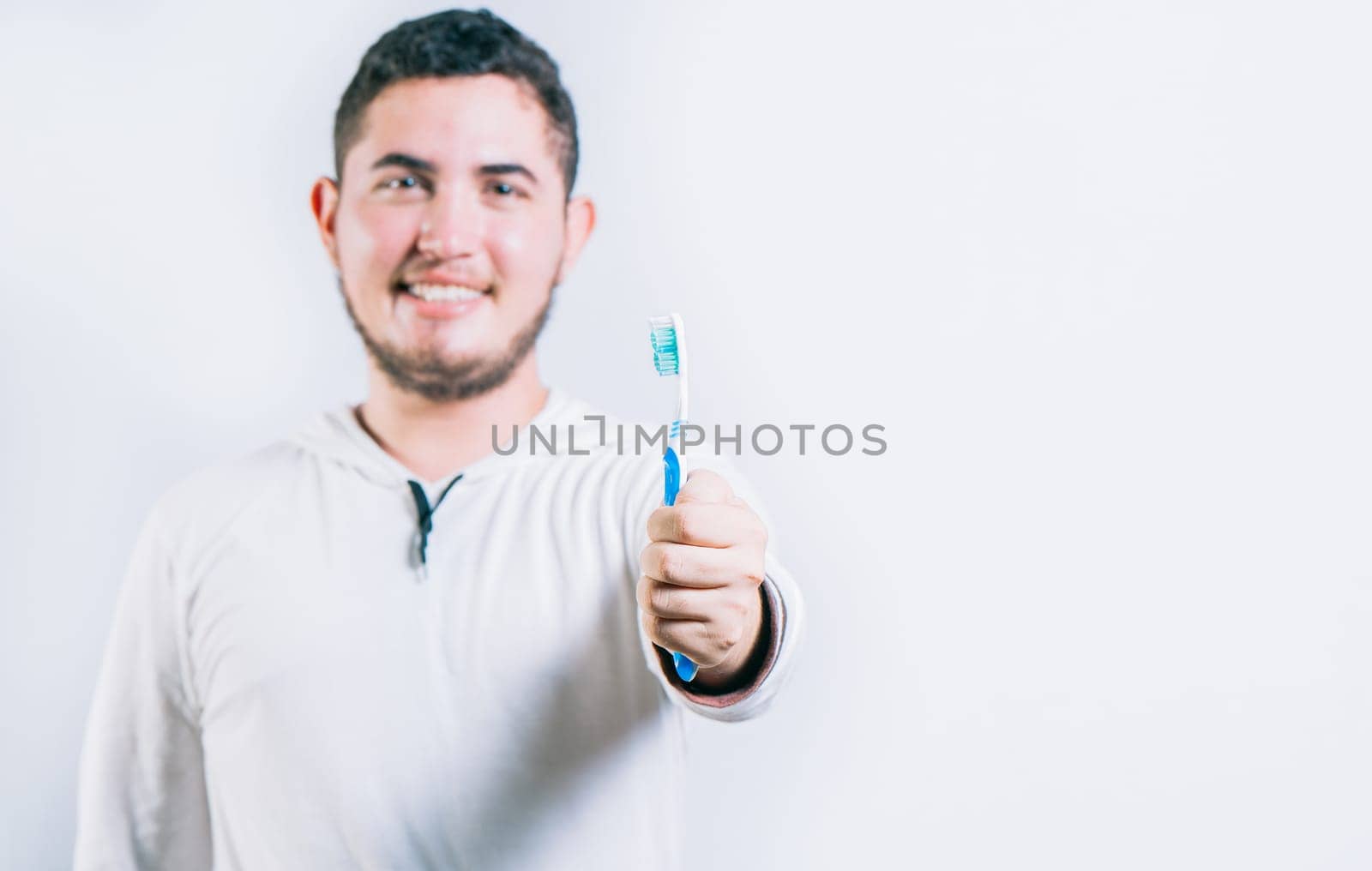 Young man holding toothbrush and looking at camera isolated. Oral health concept