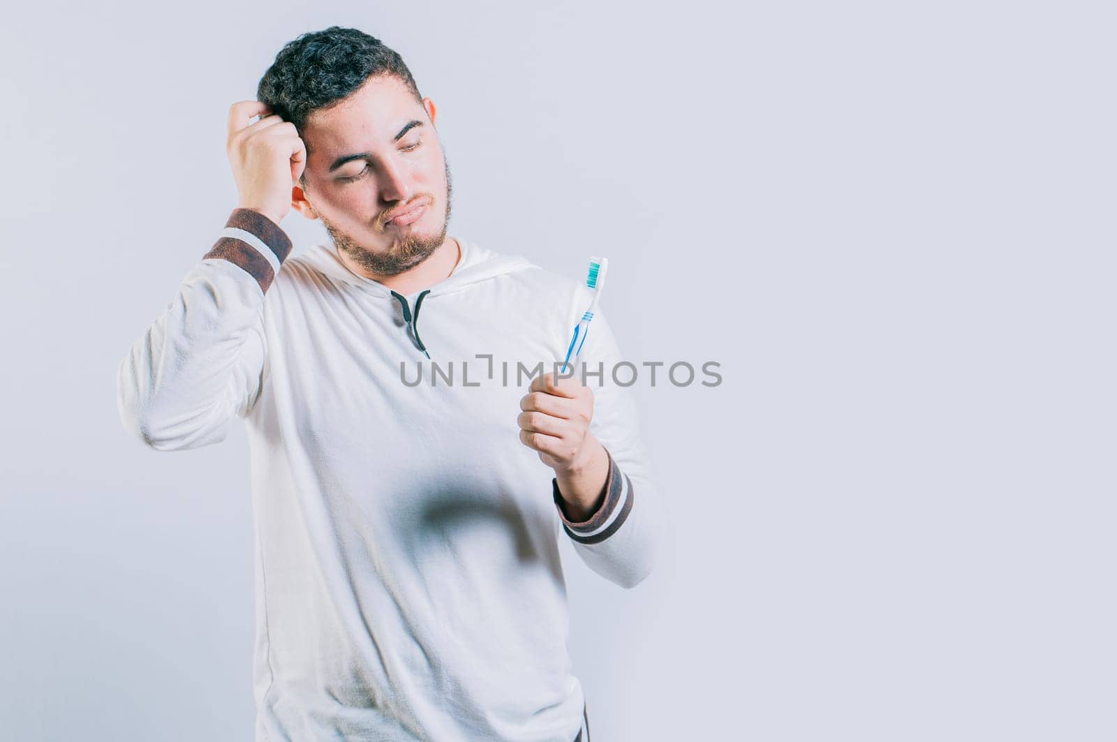 Worried young man holding toothbrush isolated. Thoughtful guy holding and looking at toothbrush isolated