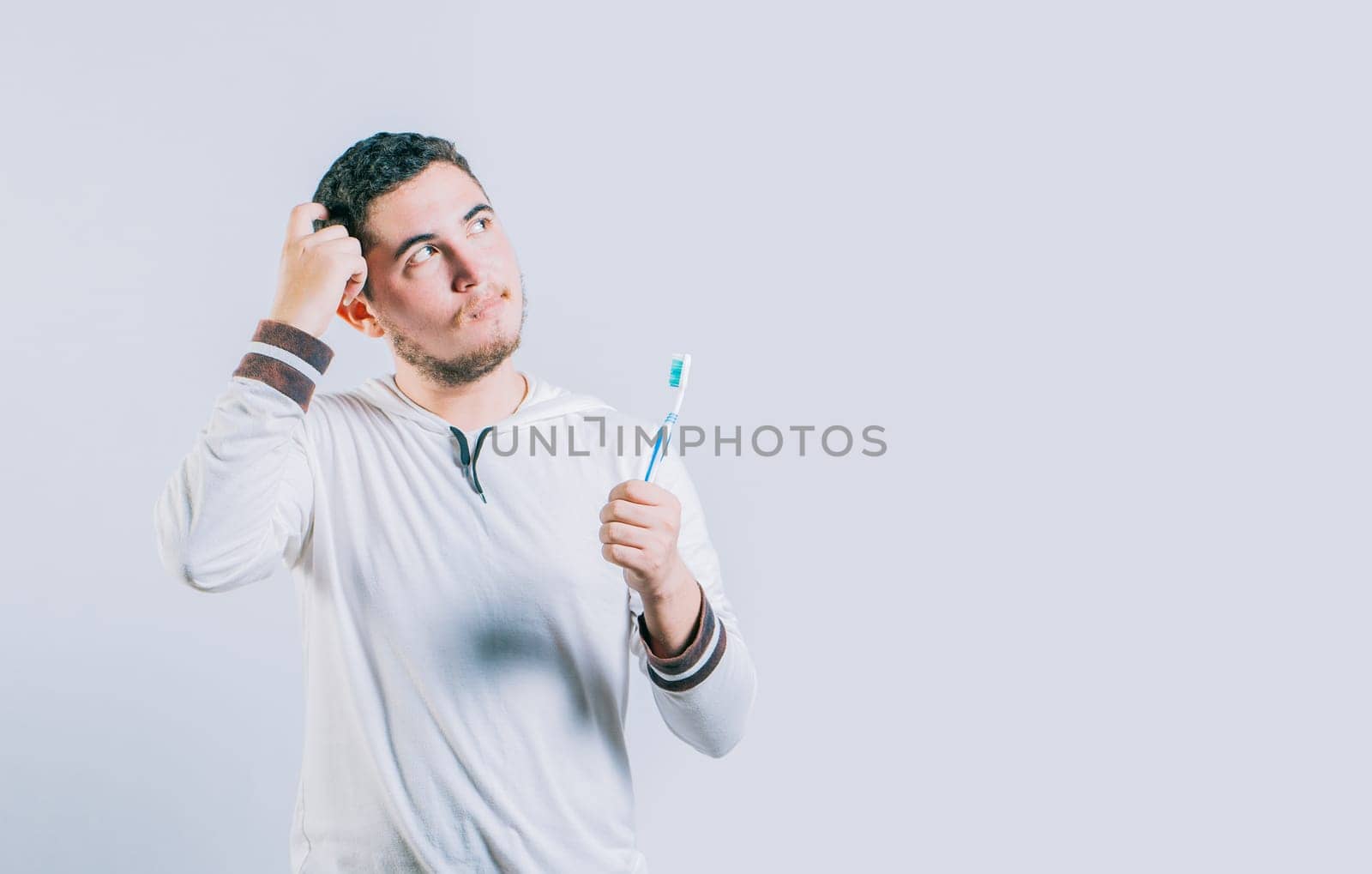 Thoughtful guy holding toothbrush looking up isolated. Worried young man holding toothbrush isolated.