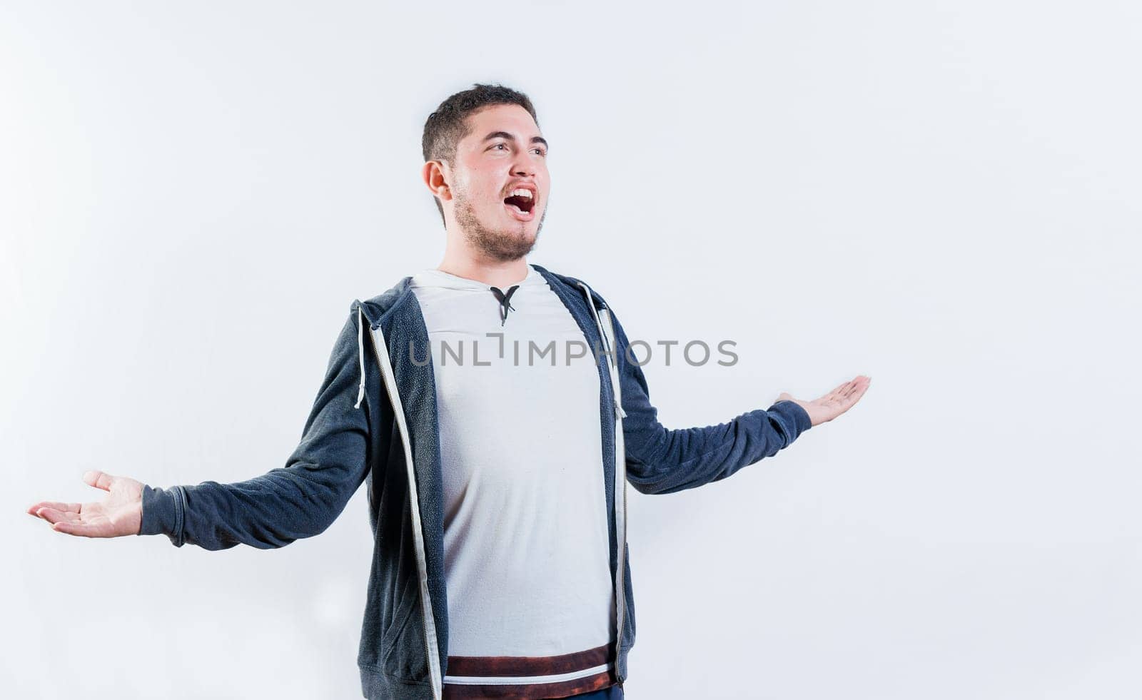 Angry young man shouting up with open hands isolated. Annoyed guy with open arms shouting isolated