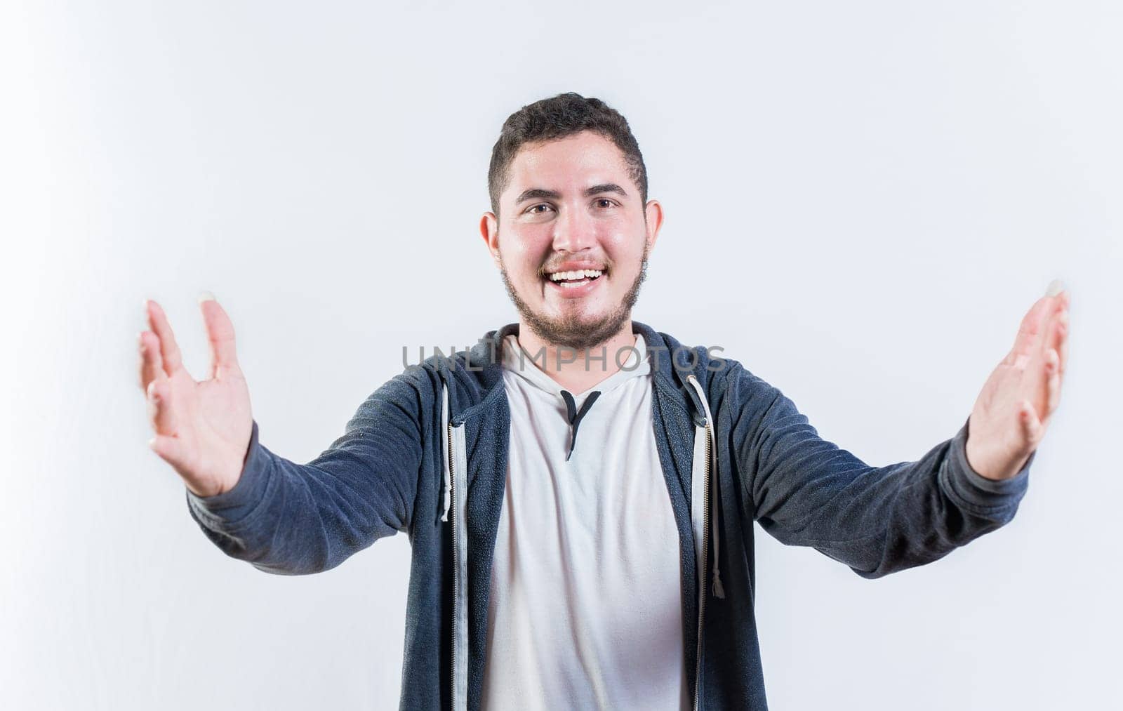 Friendly young man welcoming with open arms isolated. Hospitable guy opening arms to the camera