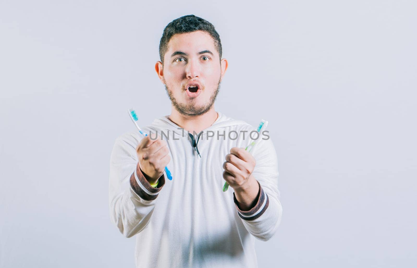 Amazed teen guy holding two toothbrush looking at camera isolated. Surprised people holding toothbrushes isolated