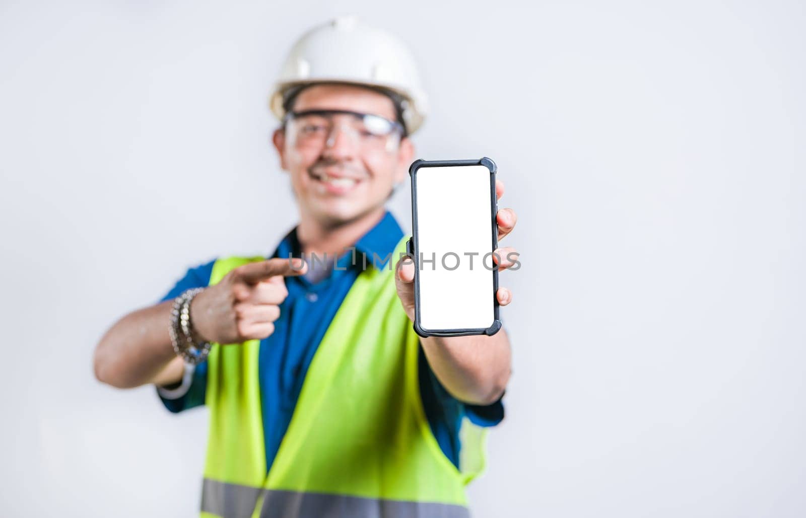 Young construction engineer showing and pointing at an advertisement on the phone screen. Happy engineer showing cell phone screen isolated