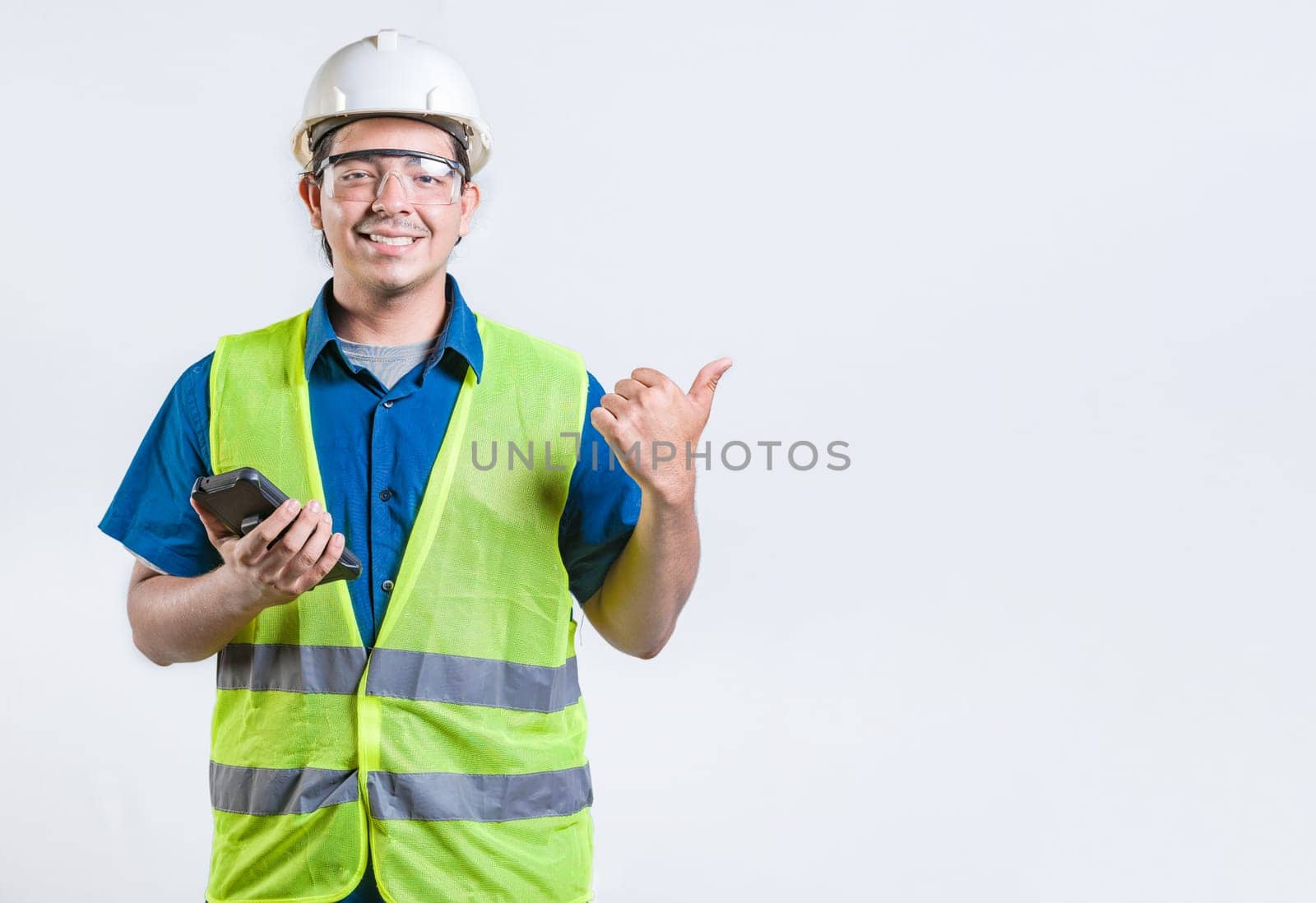 Young architect with phone pointing at blank space isolated. Smiling engineer holding phone and pointing to the side isolated