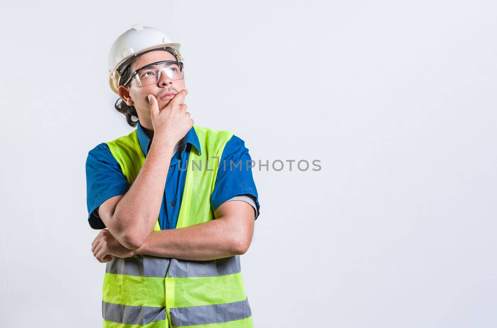 Pensive builder man with hand on chin isolated. Young builder wondering looking up with hand on chin