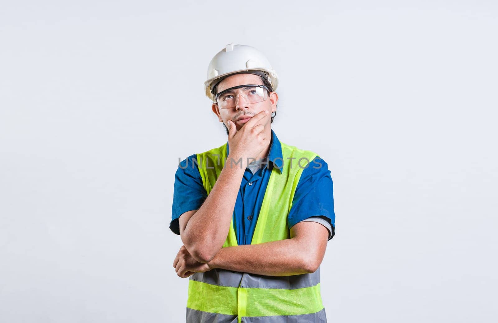 Young builder wondering looking up with hand on chin. Pensive builder man with hand on chin isolated