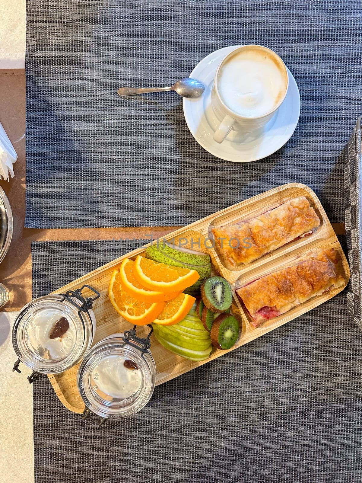 colorful breakfast spread showcases sliced fruits and pastries on a wooden tray, offering a vibrant start to the day. accompanied by glasses of water, this arrangement exudes freshness and simplicity
