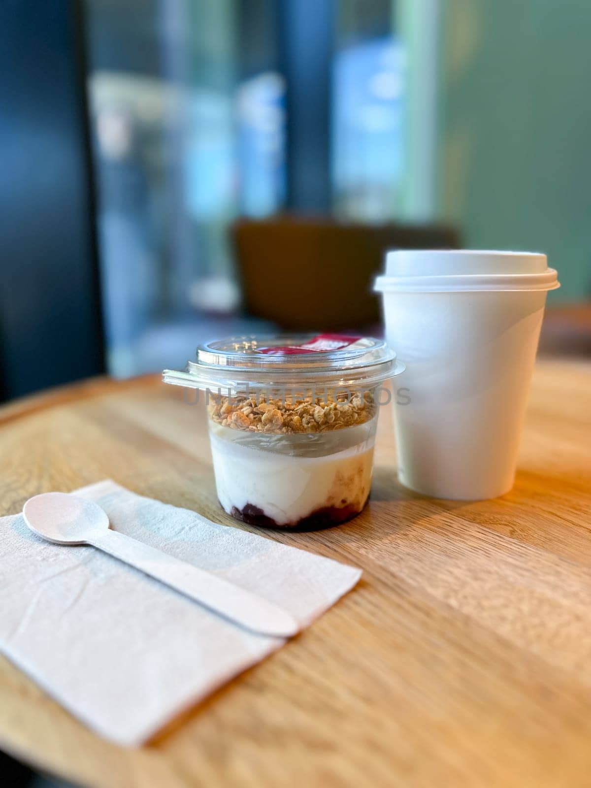 Morning breakfast of yogurt parfait with granola and a hot coffee to go in a cozy cafe setting. Relaxing and inviting atmosphere perfect for breakfast.