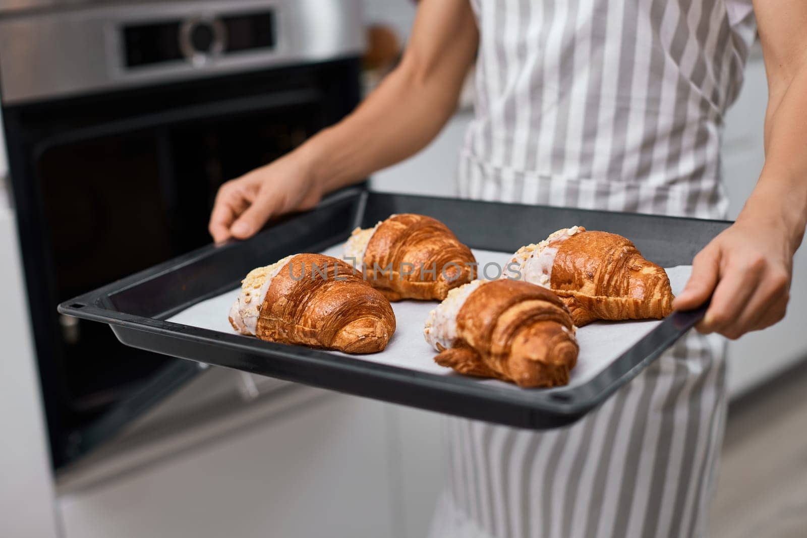 female baker holding metal tray with freshly baked crispy golden croissants