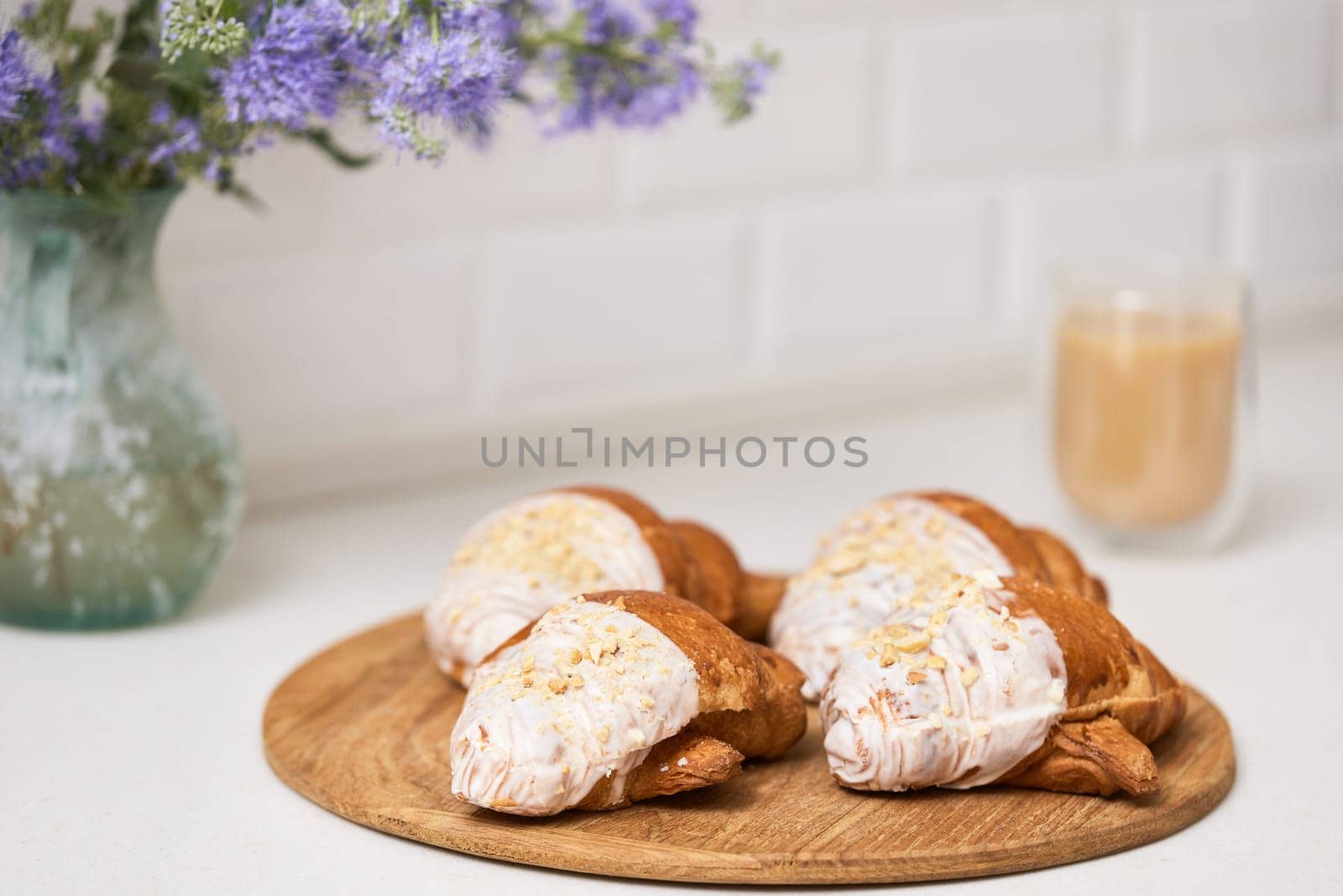 Delicious fresh croissants on wooden tray and glass of coffee on white table, closeup, tasty breakfast