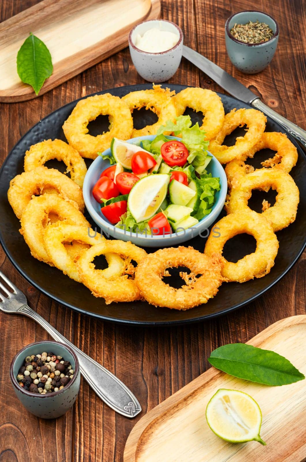 Calamari, fried squid rings with raw vegetable salad on rustic wooden table.