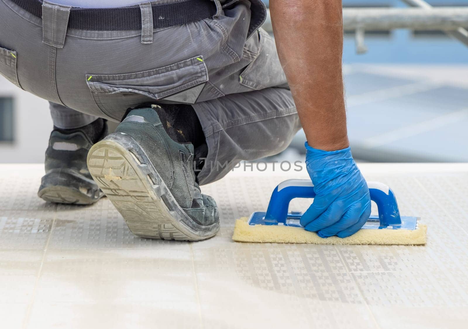 Craftsman washing surface with a float sitting on hes knees. Men in grey work clothes outside during construction or renovation process