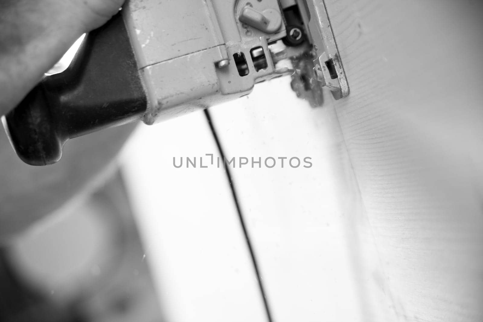 Black and white image of A carpenter is using a jigsaw to cut a board in a workshop, demonstrating his expertise in woodworking