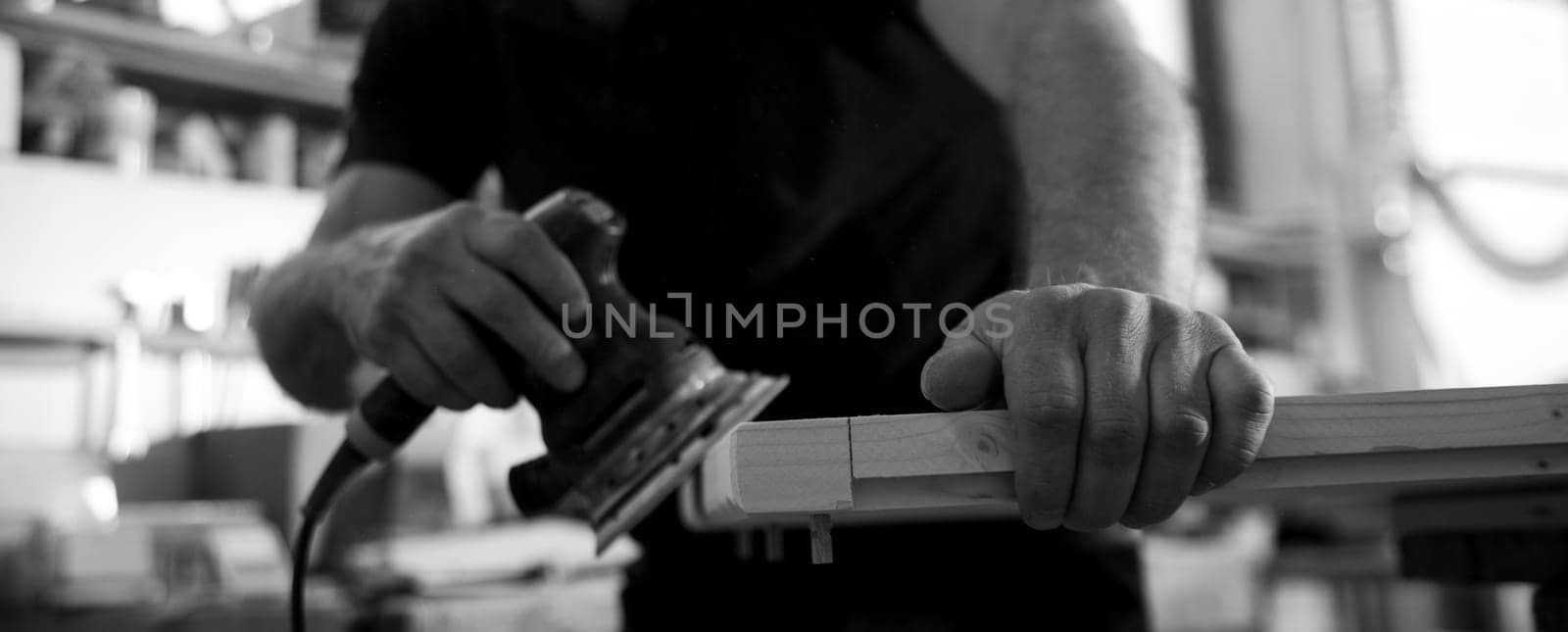 Black and white image of A carpenter is sanding a piece of wood using an electric sander in his workshop
