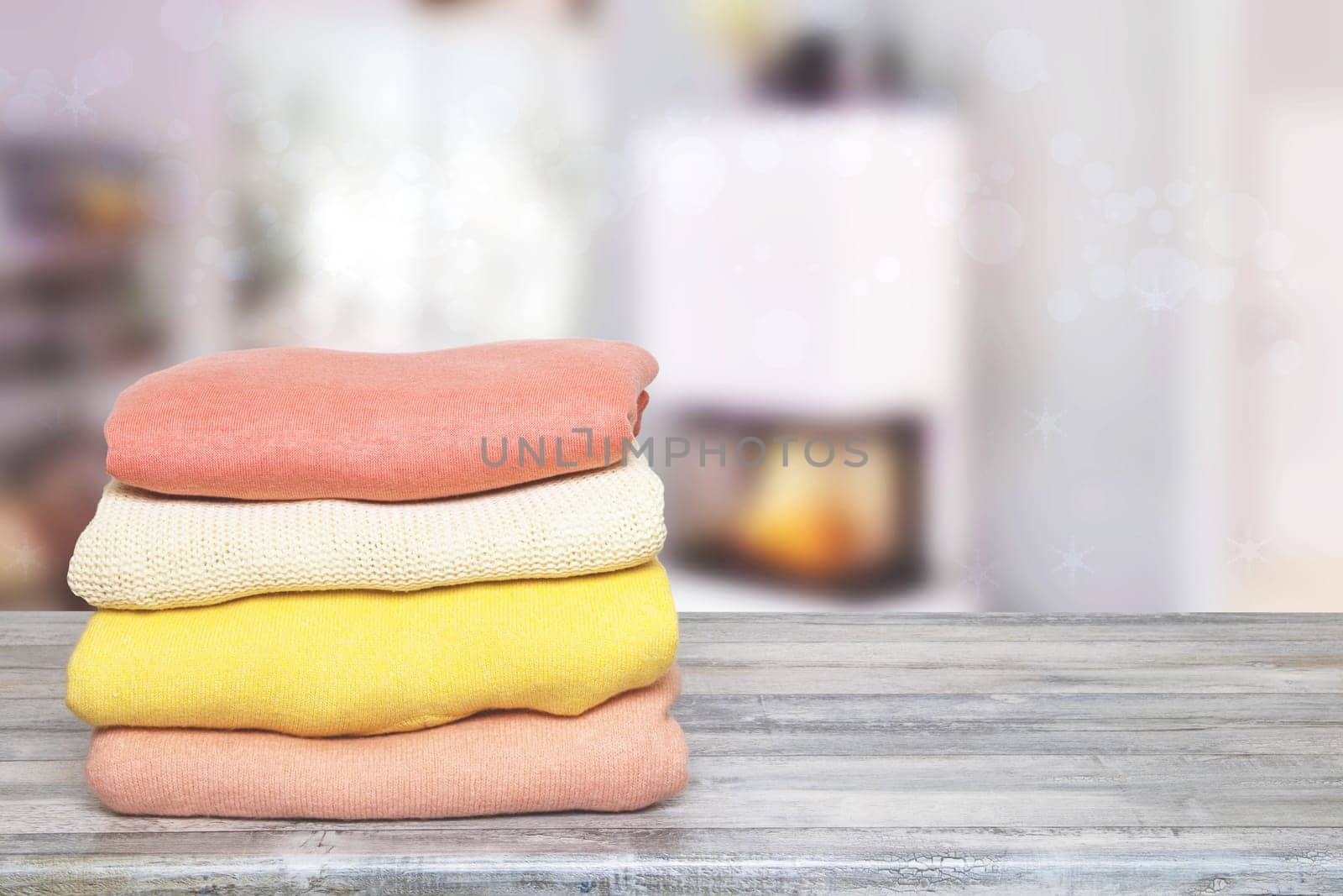 Pile of colorful knitted cozy warm cashmere sweaters on wooden table against abstract blurred living room background.Template for winter christmas sale.