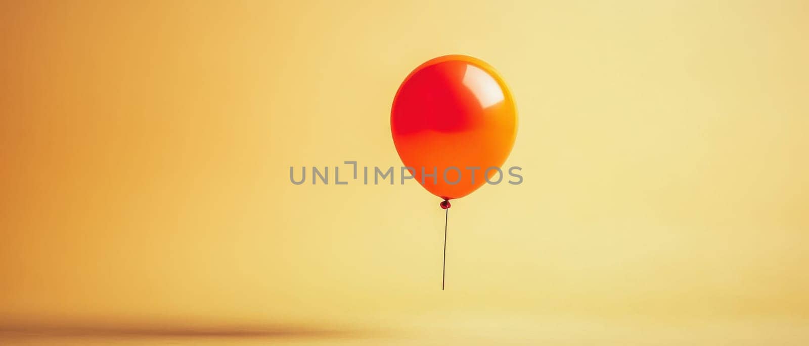 A vibrant orange balloon is suspended in mid air contrasting beautifully with a soft yellow background creating a cheerful atmosphere.