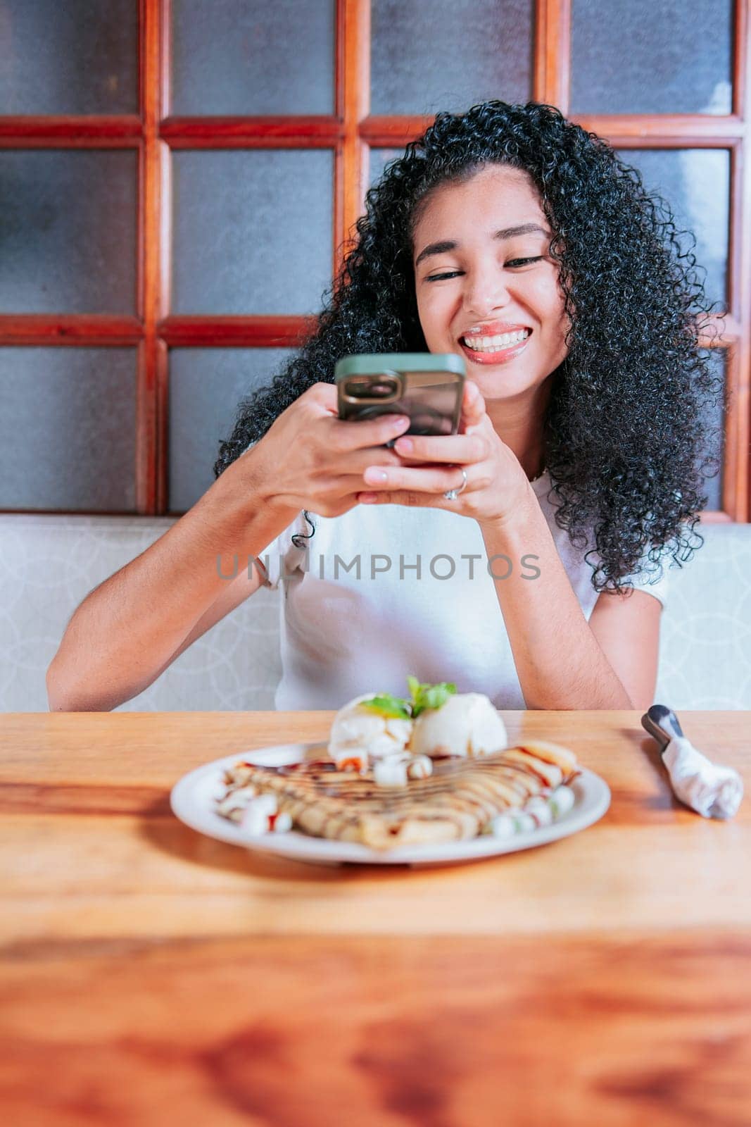 Happy girl photographing a plate of chocolate crepe and ice cream. Young woman using cell phone and taking a picture of chocolate crepe