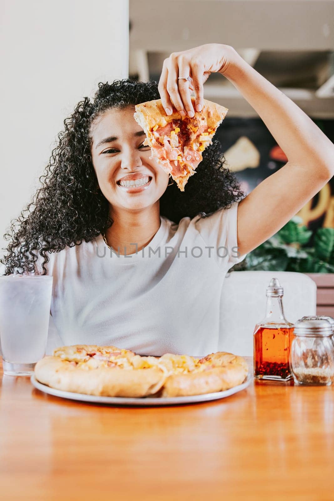Smiling afro woman enjoying a pizza in a restaurant. Happy afro hair woman showing slice of pizza in a restaurant