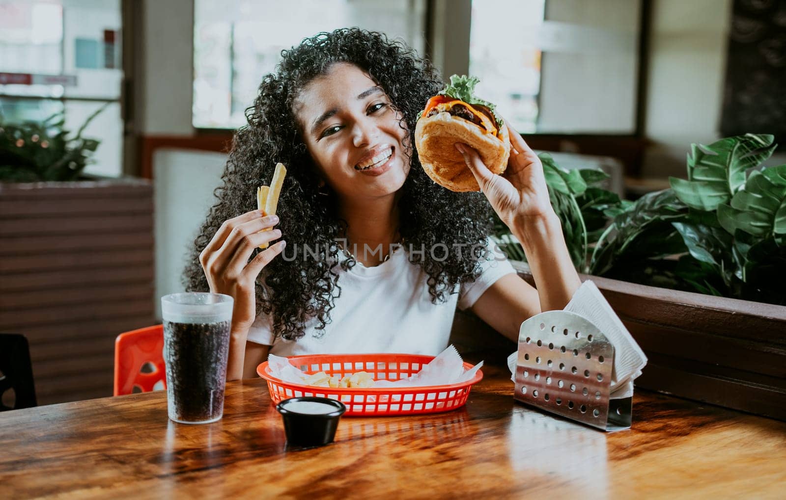 Afro young woman enjoying a hamburger with fries in a restaurant. Happy girl enjoying a hamburger in a restaurant
