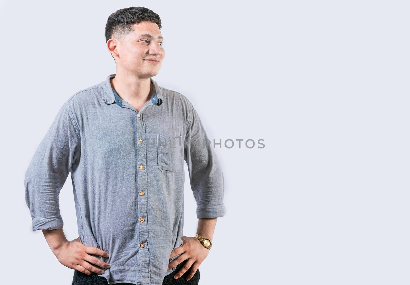 Satisfied young man with hands on hip looking to side. Young man with hands on hips looking at an advertisement to the side