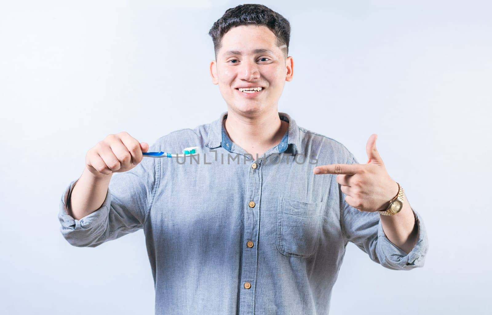Man holding and recommending a toothbrush. Smiling guy holding and pointing at toothbrush isolated. Happy person showing and pointing at toothbrush