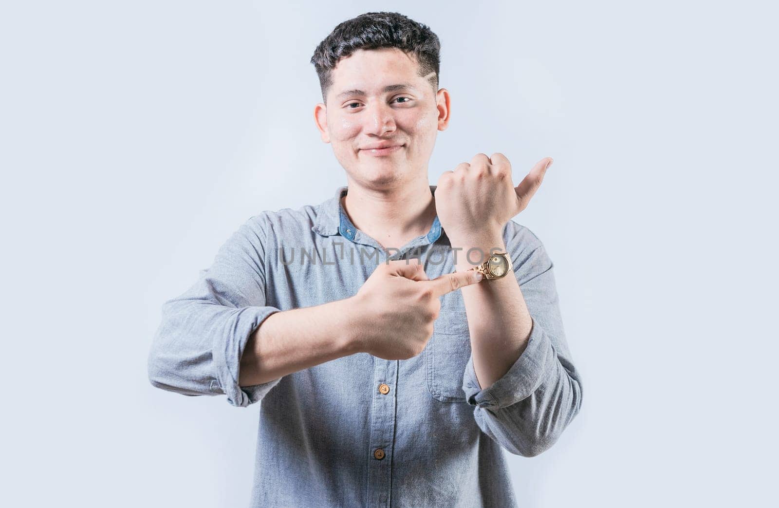 Smiling young man pointing at his wrist watch isolated. Portrait of person pointing his wrist watch on isolated background
