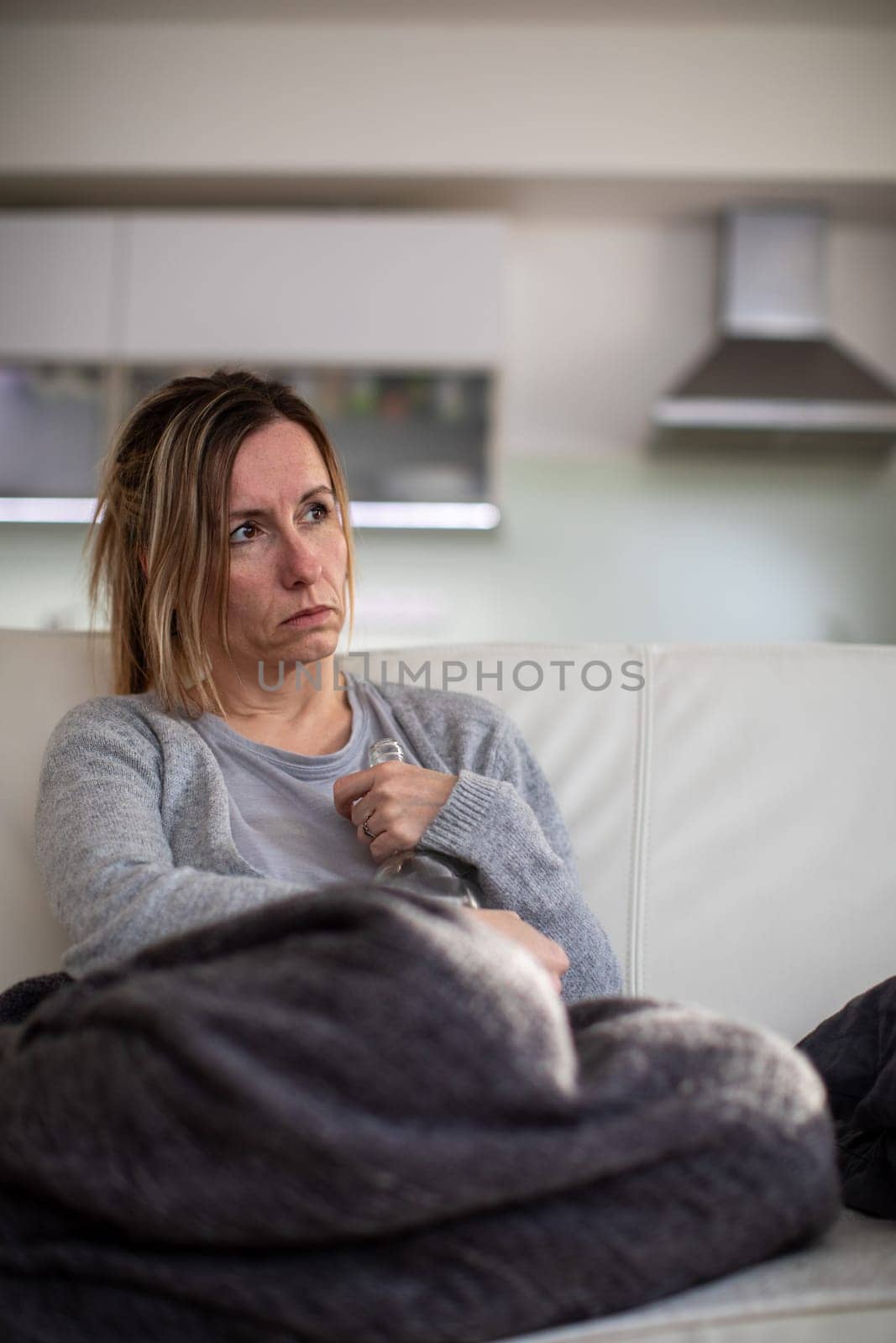 Midlle aged woman at home with a bottle of strong alcohol in her hands, dealing with depression, pain, loneliness