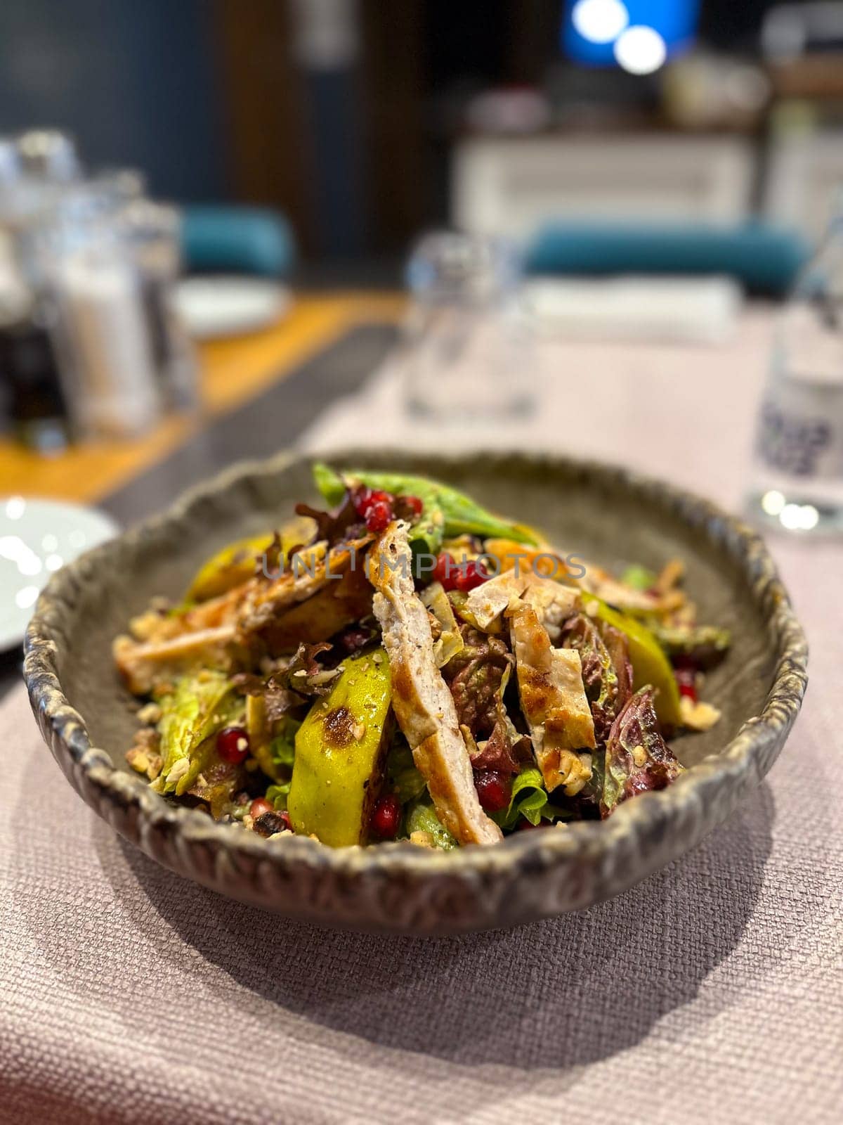 Vibrant salad is artfully presented in a rustic bowl, featuring grilled chicken, fresh greens, avocado slices, pomegranate seeds, and crunchy nuts. Appetizing dish highlights a colorful and healthy dining option perfect for any gourmet experience top view.