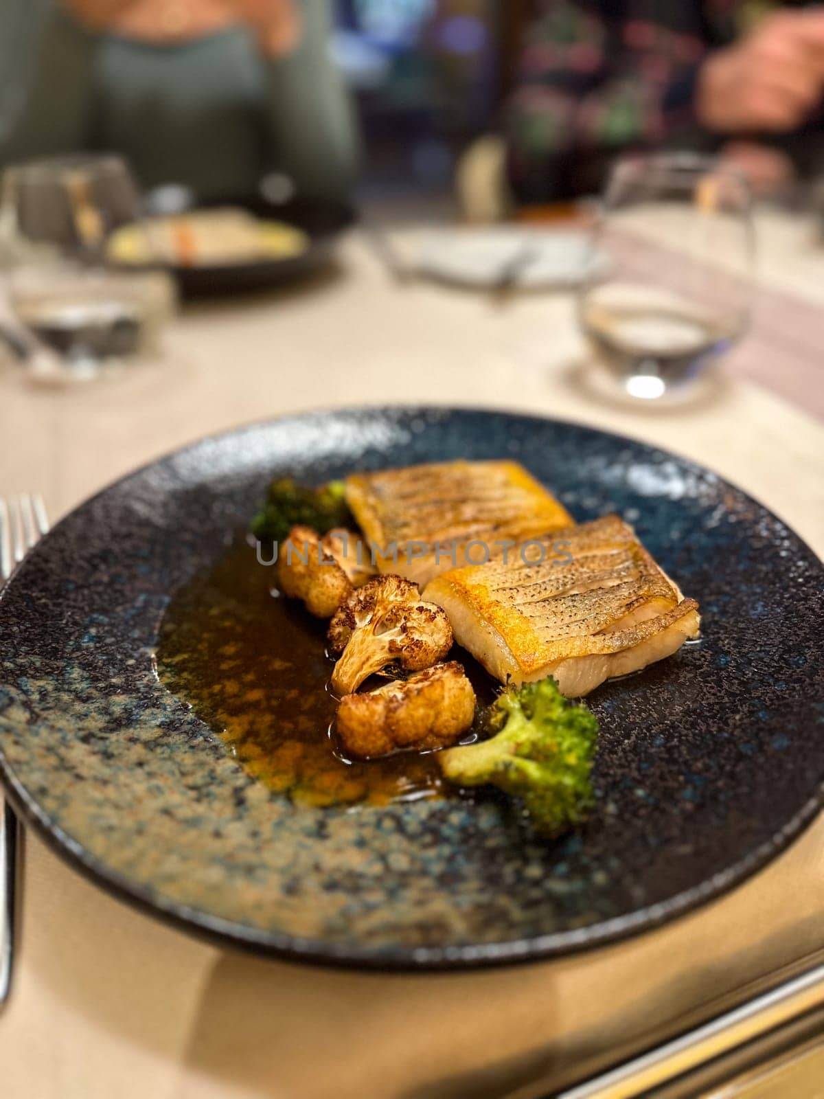 Plated gourmet dish features succulent fish fillets accompanied by roasted cauliflower and broccoli, set against a rich, dark sauce. this image captures an exquisite dining experience, showcasing the artistry of haute cuisine.