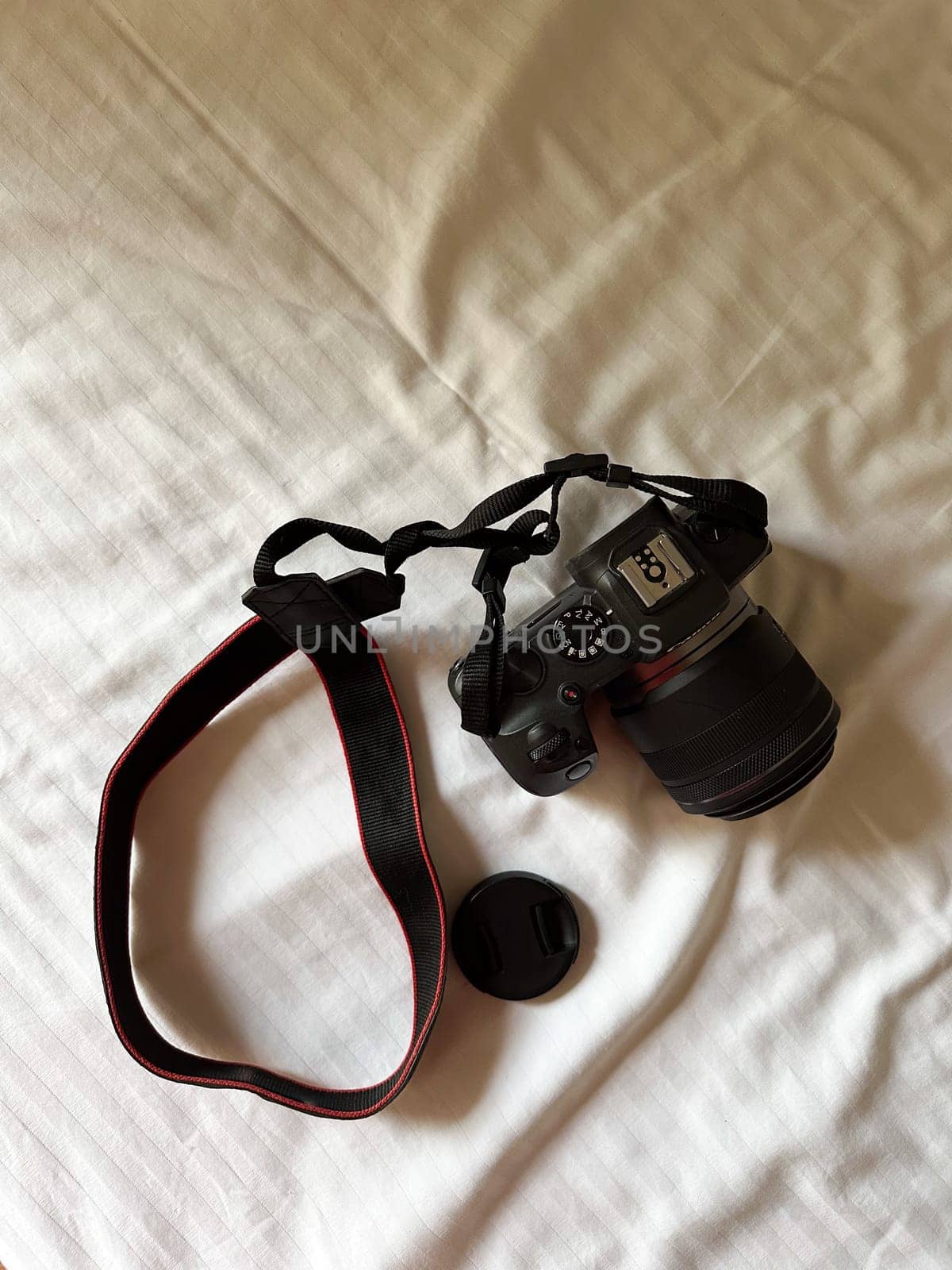 Camera with a strap placed on a white bed sheet, capturing the essence of travel preparation and creativity. Simplicity, creative and readiness of a photographer journey.