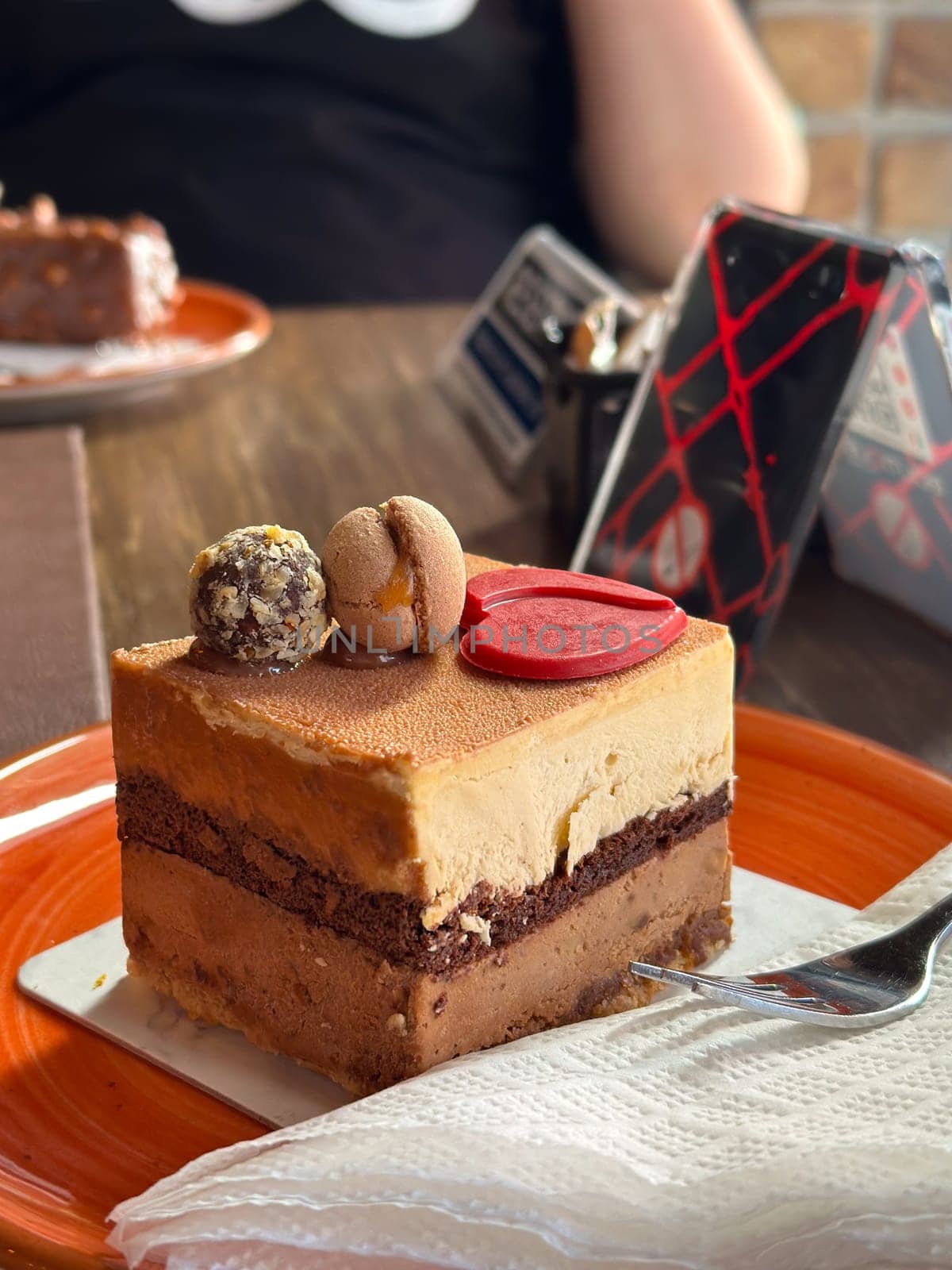Close-up of a delicious chocolate mousse cake with macaron and truffle topping on an orange plate. Concept of indulgence and delight sweets in a cozy cafe setting