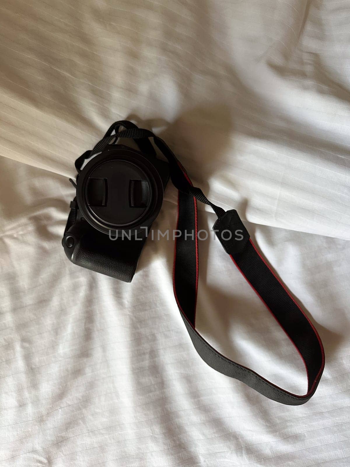 Camera with a strap placed on a white bed sheet, capturing the essence of travel preparation and creativity. Simplicity, creative and readiness of a photographer journey.