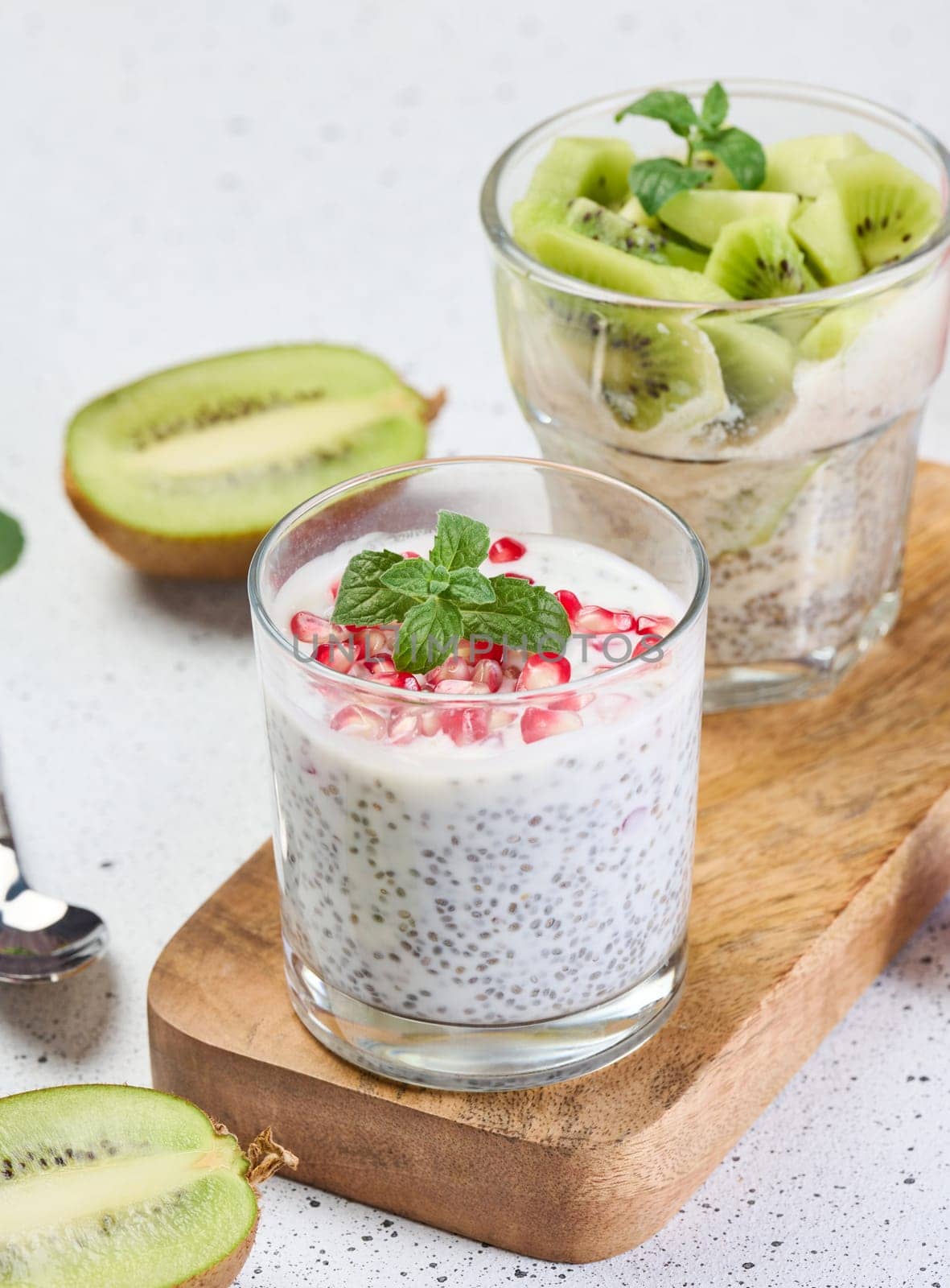 Two glasses of chia yogurt dessert garnished with fresh fruit, pomegranate seeds and kiwi slices
