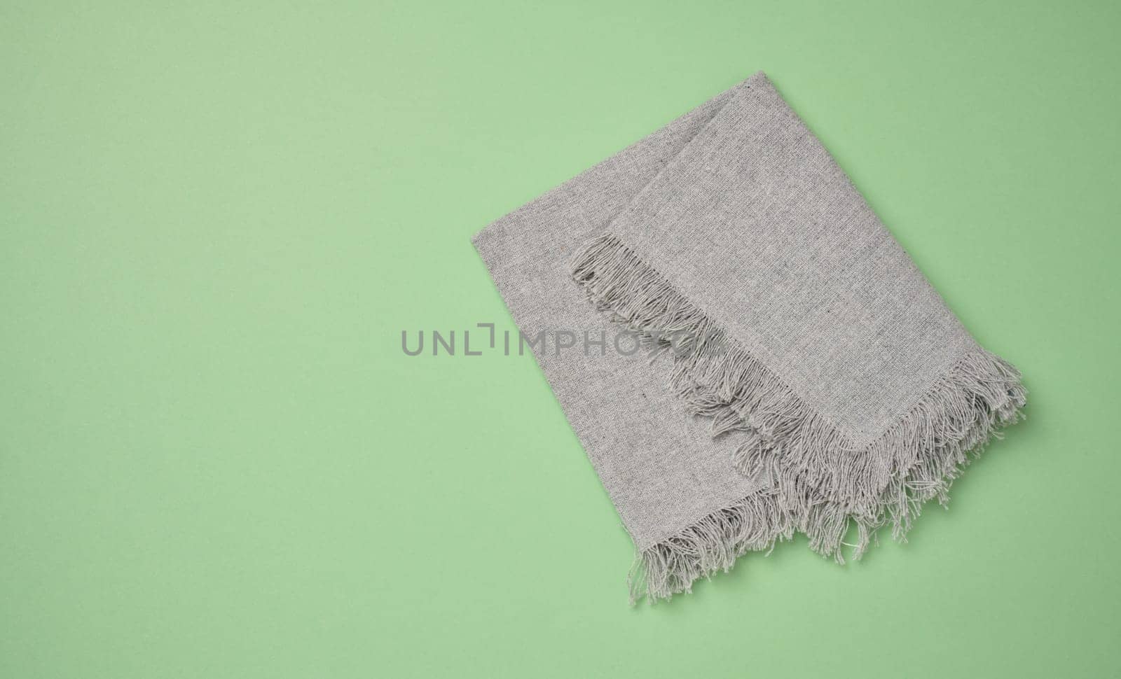 Folded gray kitchen towel on a green background, top view. Copy space