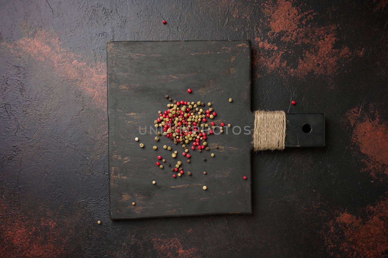 Mixture of red, green and black peppercorns on a wooden board, top view