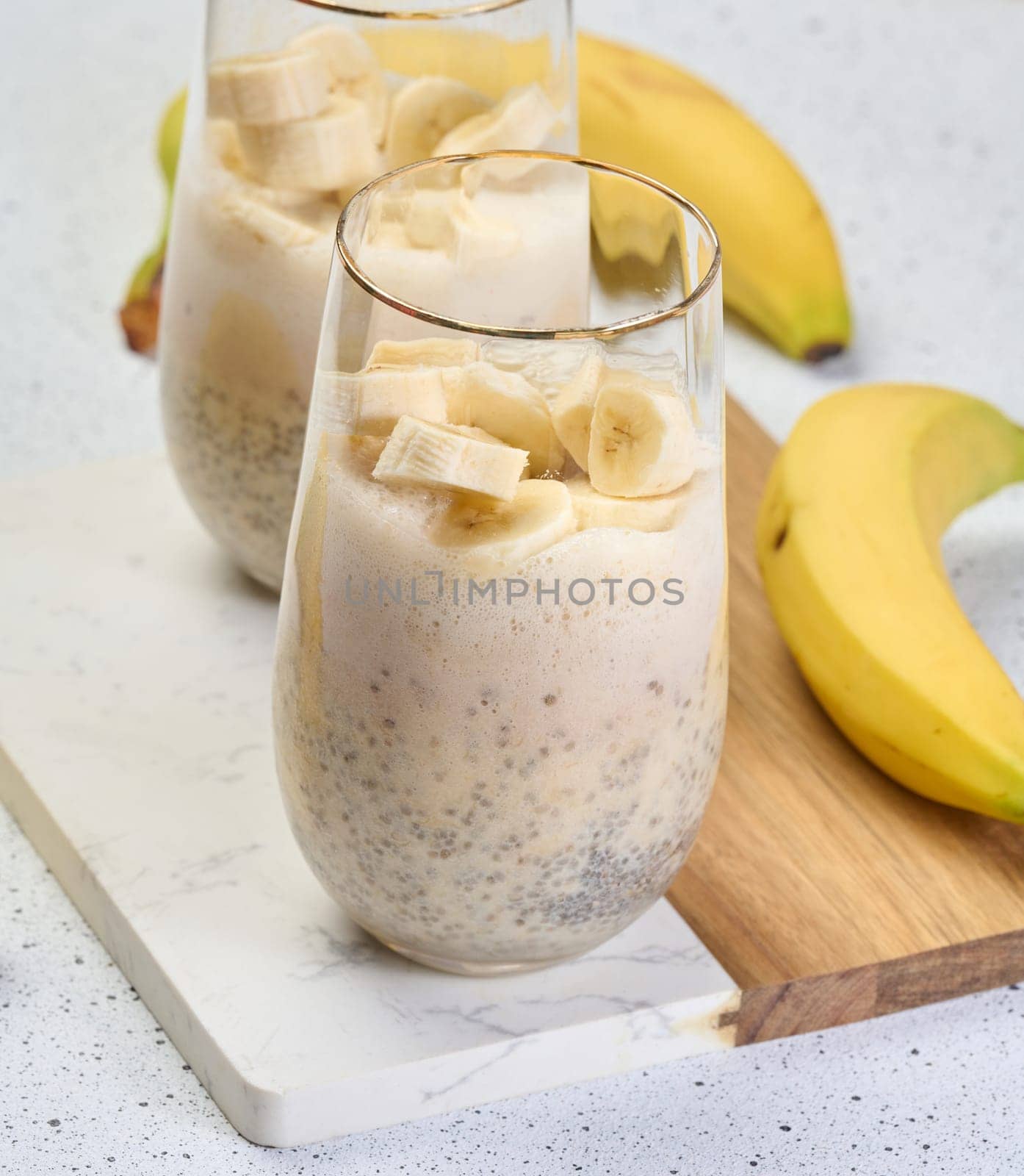 Glass with chia and yogurt dessert garnished with fresh banana slices on white table