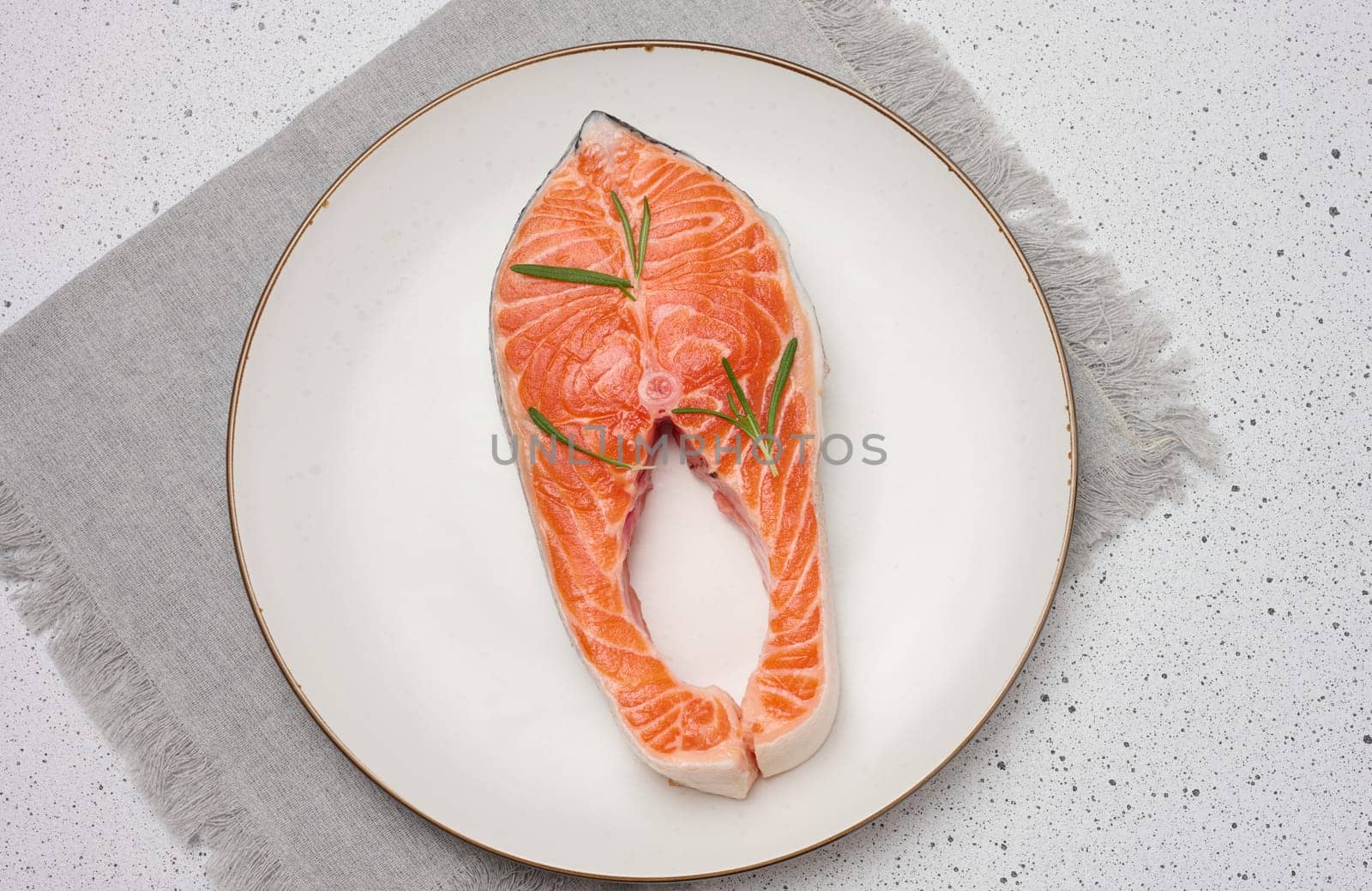 Raw piece of salmon fish steak in round white plate on white background, top view