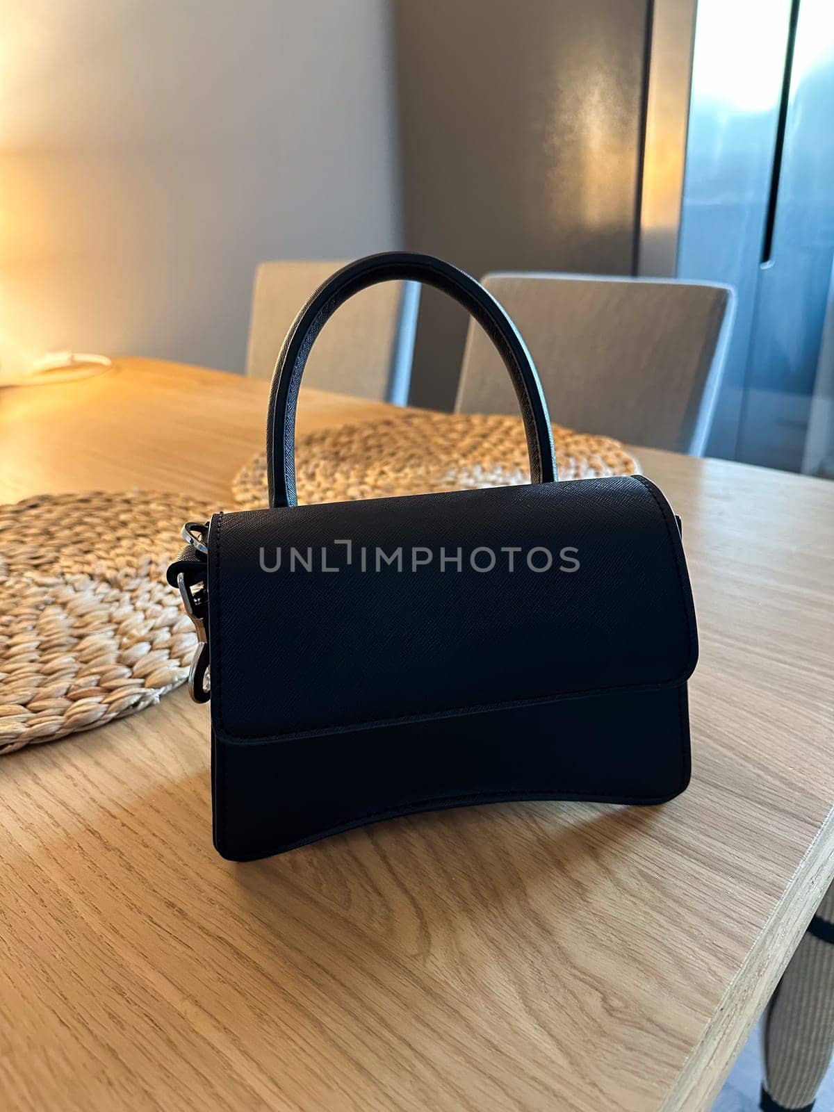 Stylish fashion black handbag placed elegantly on a wooden table. Soft lighting creates a warm atmosphere, highlighting the design and texture of the purse.